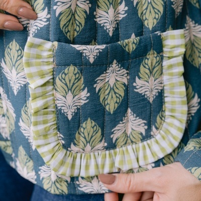 Peça de vestuário azul com padrão de folhas e bolso com frisos xadrez verde e branco