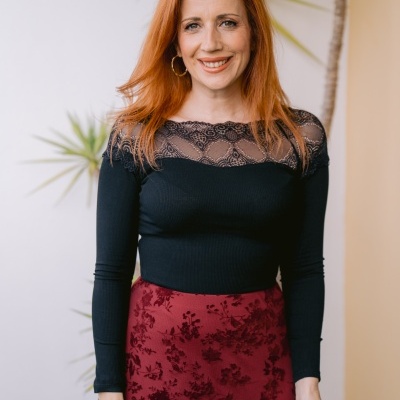 Mulher de blusa preta com renda e saia vermelha com padrão floral perto de plantas