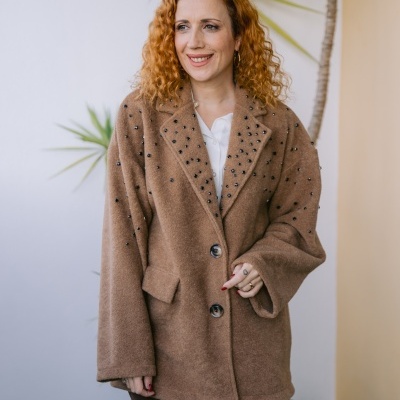 Casaco castanho com cristais pretos usado por mulher com camisa branca e calças castanhas