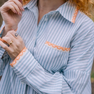 Camisa de algodão às riscas azuis e brancas com bordados laranja nas bordas e botões brancos.