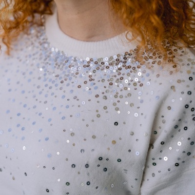 Suéter branco com lantejoulas prateadas e cabelo ruivo encaracolado