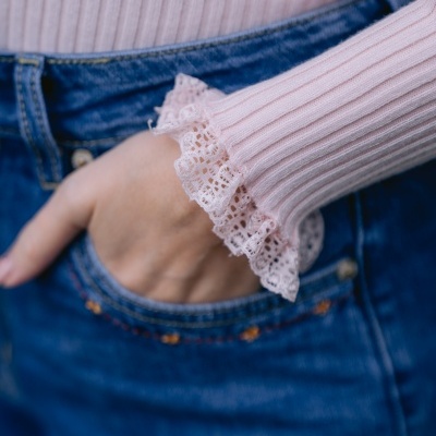 Manga de camisola rosa clara canelada com renda e calças de ganga azul com mão no bolso.