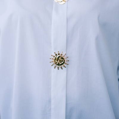 Camisa branca com botões decorativos dourados em forma de flor, sol e estrela-do-mar.