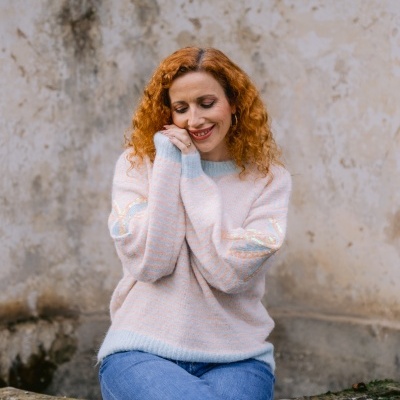 Mulher com camisola listrada rosa e azul claro sentada num banco de pedra