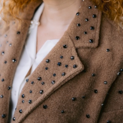 Casaco castanho felpudo com pedras pretas redondas aplicadas, usado sobre camisa branca