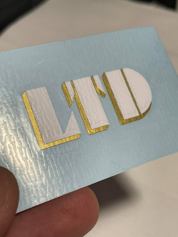 LTD Logo em Vinil Cartão azul claro texturizado com letras brancas em relevo e bordas douradas LWD