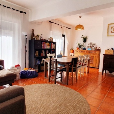 Sala de estar e jantar com sofá castanho, mesa de madeira clara e estantes com objetos decorativos