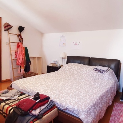 Quarto com cama de couro preto, edredão branco, mesas pretas, tapete vermelho e cabideiro com roupa.