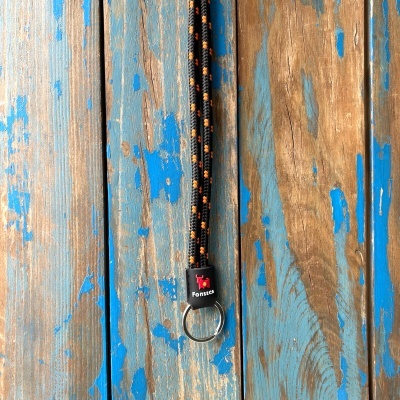 Cordão trançado preto com pontos laranja e etiqueta Fonseca numa superfície de madeira azul e castanha