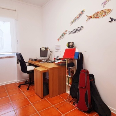 Escritório com secretária de madeira, cadeira preta, guitarra vermelha em capa preta e decoração de peixes na parede branca