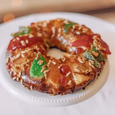 Rosca doce decorada com frutas cristalizadas e pinhões num prato branco.