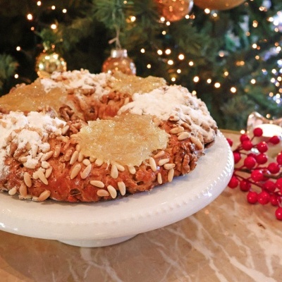 Bolo natalício decorado com pinhões e doce numa base branca sobre uma mesa de mármore