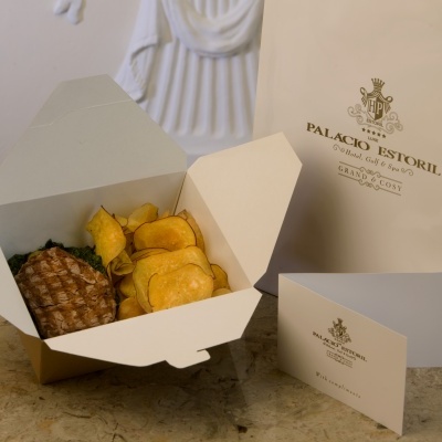Caixa aberta com batatas fritas e waffle, saco e cartão do Palacio Estoril