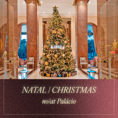 Árvore de Natal decorada com luzes e bolas douradas num salão com colunas de mármore vermelho