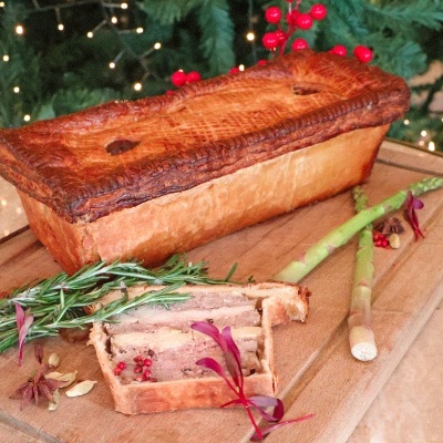 Patê de carne em forma de bolo com ervas e aspargos numa tábua de madeira