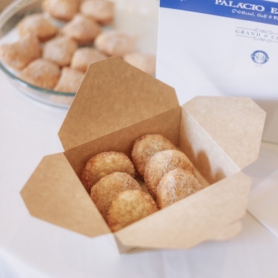 Caixa de cartão castanha com biscoitos redondos cobertos com canela e açúcar, embalagem branca e azul ao fundo