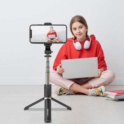 Rapaz jovem com portátil sentado no chão com tripé e smartphone em frente