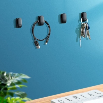 Ganchos pretos na parede azul segurando cabo USB e chaves, mesa de madeira clara com planta