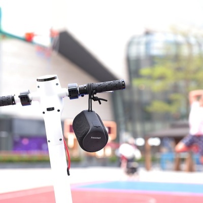 Scooter elétrico branco com coluna portátil preta Anker pendurada no guiador ao ar livre