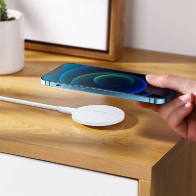 Carregador sem fios branco com telemóvel azul sobre mesa de madeira