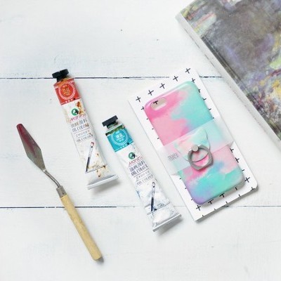 tubos de tinta óleo, espátula e capa de telemóvel colorida sobre superfície branca