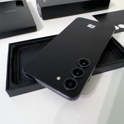 Smartphone preto com três câmaras traseiras e caixa preta em mesa branca