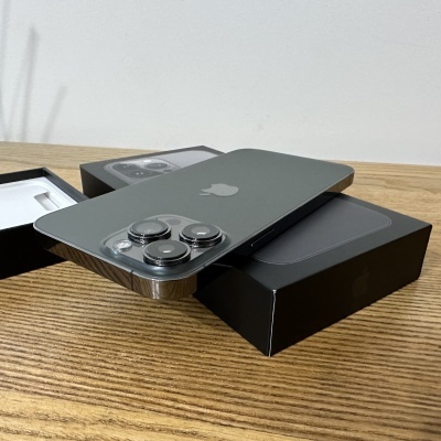 Smartphone Apple iPhone com três câmaras em cima de caixas pretas numa mesa de madeira.