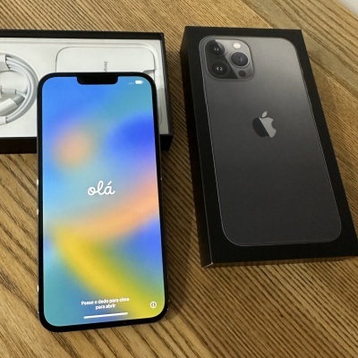 Smartphone Apple iPhone preto com ecrã a mostrar o texto olá, caixa do iPhone e acessórios sobre mesa