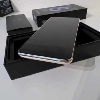 Smartphone com ecrã preto e bordas prateadas em caixa preta aberta com caixa de fundo com 'S' roxo e folheto Samsung