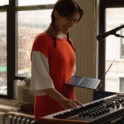 Mulher a tocar teclado musical preto com tablet em mãos junto a janela grande