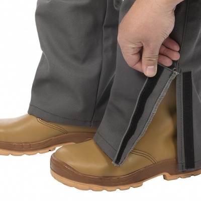 Calças cinzentas com fecho e velcro na bainha junto a botas castanhas.