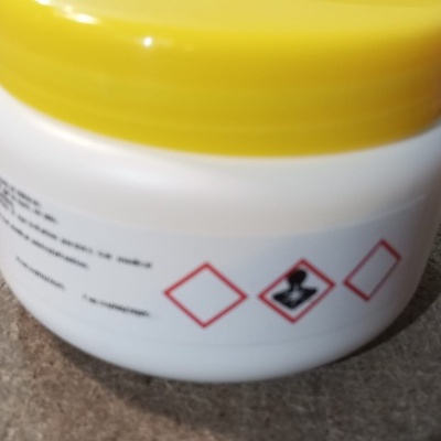 Frasco plástico branco com tampa amarela e símbolos de perigo químicos no rótulo
