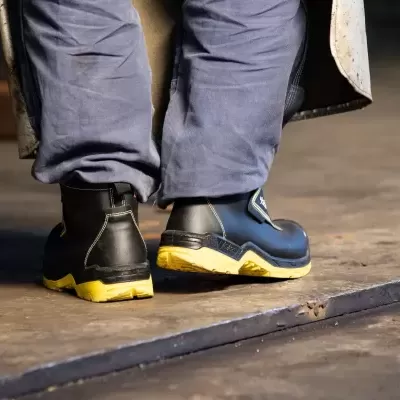 Calçado de segurança azul e preto com sola amarela em chão de madeira