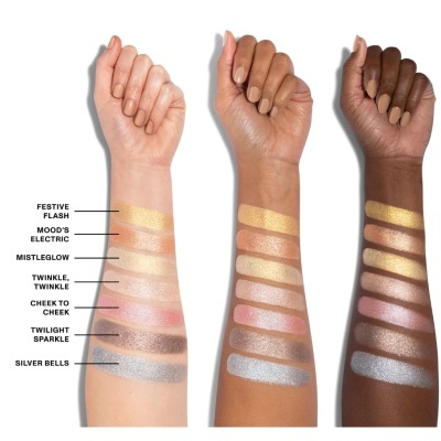 Três braços com diferentes tons de pele exibindo amostras de maquilhagem em faixas horizontais coloridas e brilhantes com nomes ao lado.