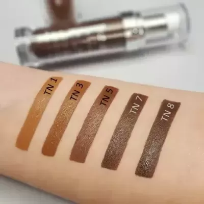 Amostras de cinco tons de bastão de maquiagem castanho em pele, com embalagem transparente ao fundo.