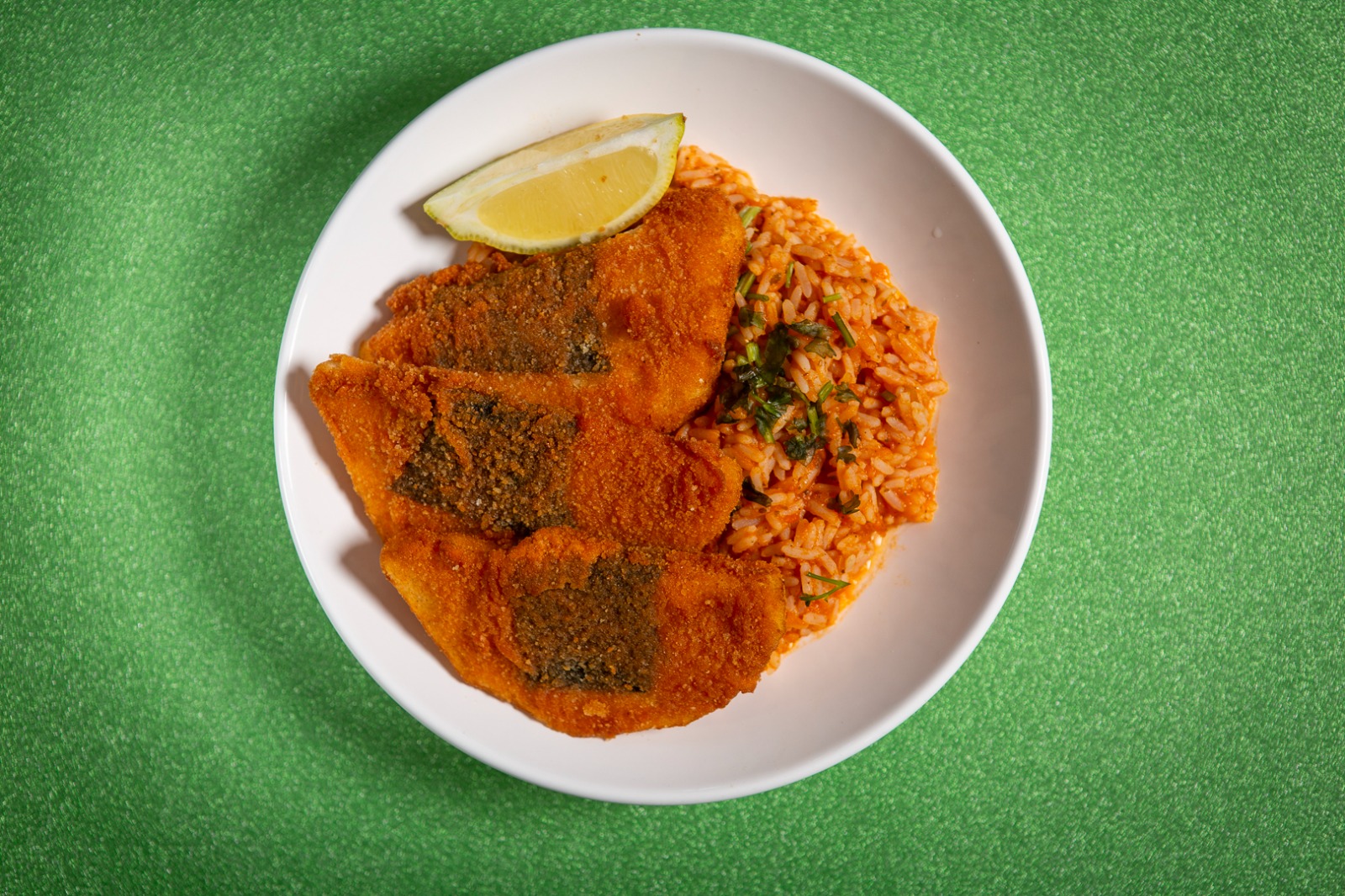 Pataniscas de aipo e nori com risotto de tomate e coentros Prato com pão empanado, arroz e limão sobre mesa verde