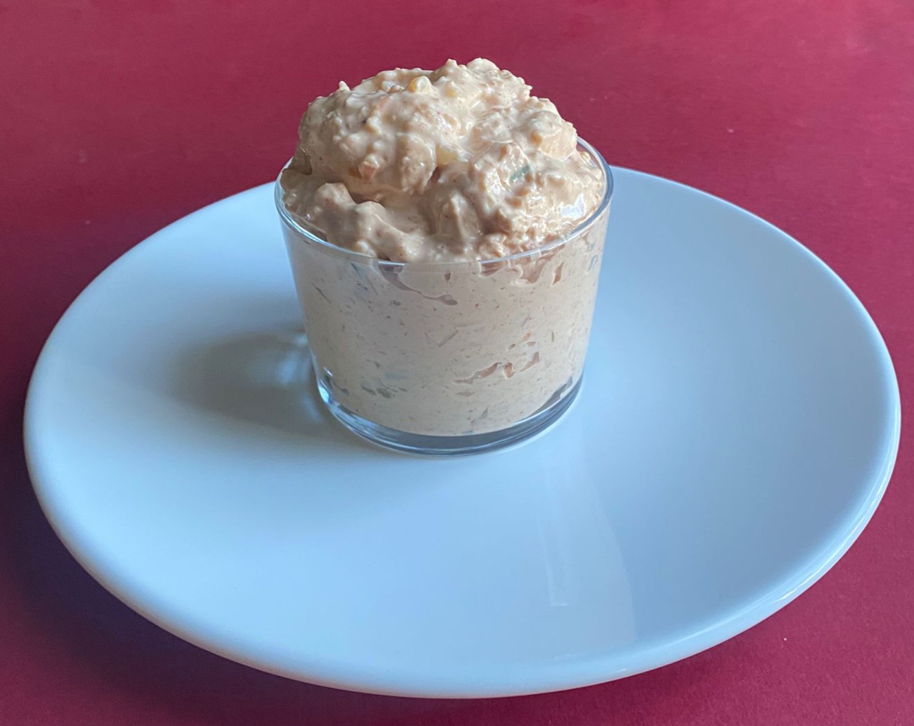 Paté de 'atum' vegano 300g Pasta cremosa rosada num copo de vidro sobre prato branco e fundo vermelho