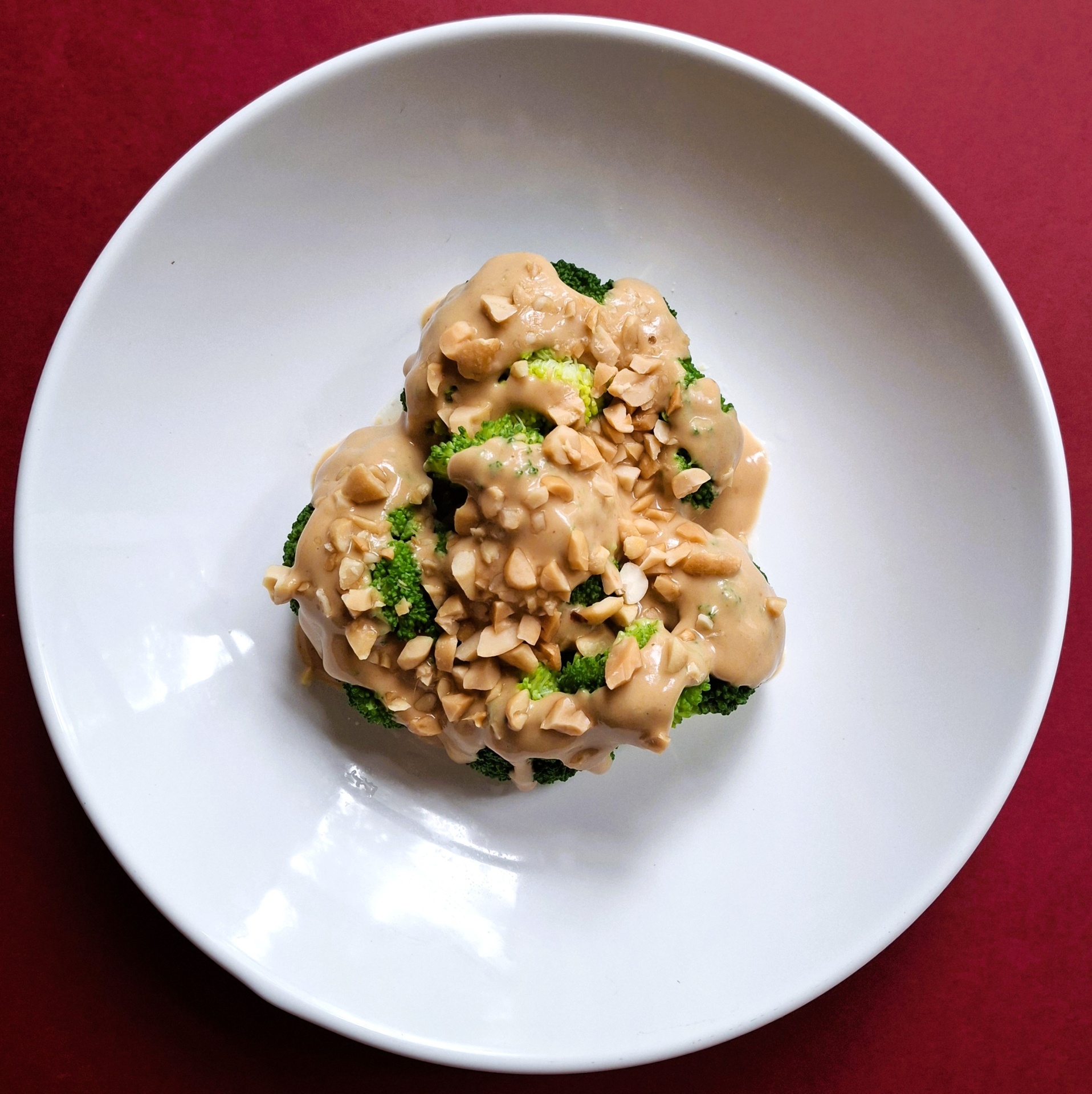 Brócolos c molho de amendoim Prato branco com brócolos e molho cremoso com pedaços de nozes