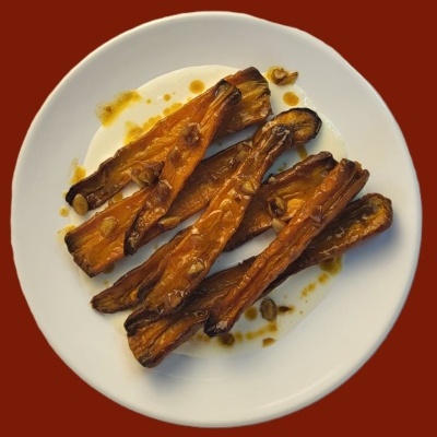 Prato branco com beringelas assadas em tiras numa superfície vermelha