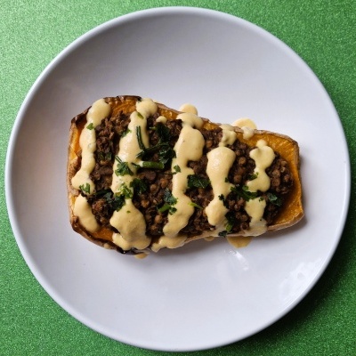 Metade de abóbora assada recheada com lentilhas, coberta por molho e ervas num prato branco