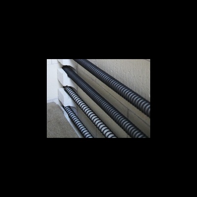 Quatro tubos corrugados de plástico pretos e branco apoiados no chão junto a uma parede clara