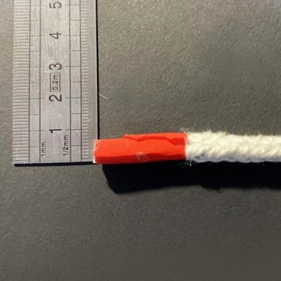 Fio branco trançado com ponta vermelha ao lado de régua metálica