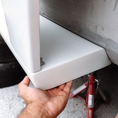 Para-choques branco de automóvel junto a macaco hidráulico vermelho no chão cinzento