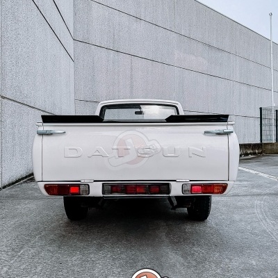 Traseira de pickup branca Datsun com spoiler preto e logótipo em relevo numa área de betão