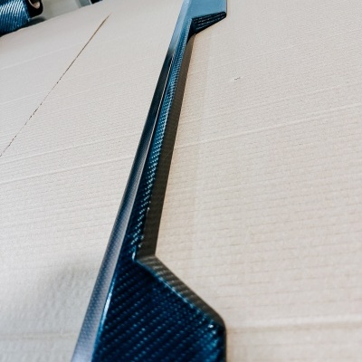 Barra longa de fibra de carbono preta com padrão entrelaçado sobre cartão castanho.