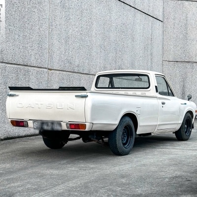 Carrinha pick-up Datsun branca estacionada junto a paredes cinzentas de betão