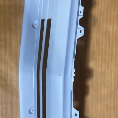 Peça branca de automóvel com encaixes sobre superfície de madeira clara