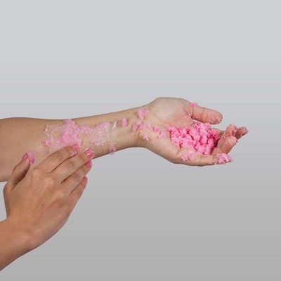 Mão segurando espuma rosa contra fundo cinza