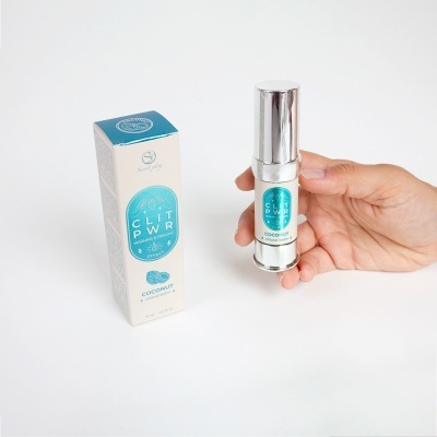 Spray íntimo CLIT PWR de embalagem metálica prateada e caixa branca com azul, segurado por mão