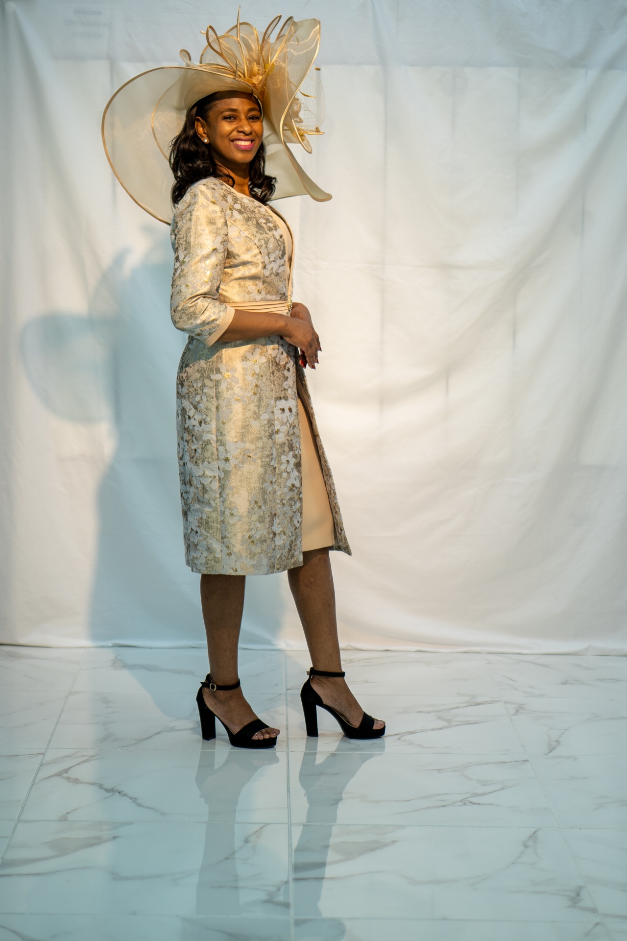 JM2305 - Fato de Senhora Mulher com vestido bege, casaco dourado estampado, sapatos pretos de salto e chapéu bege decorativo